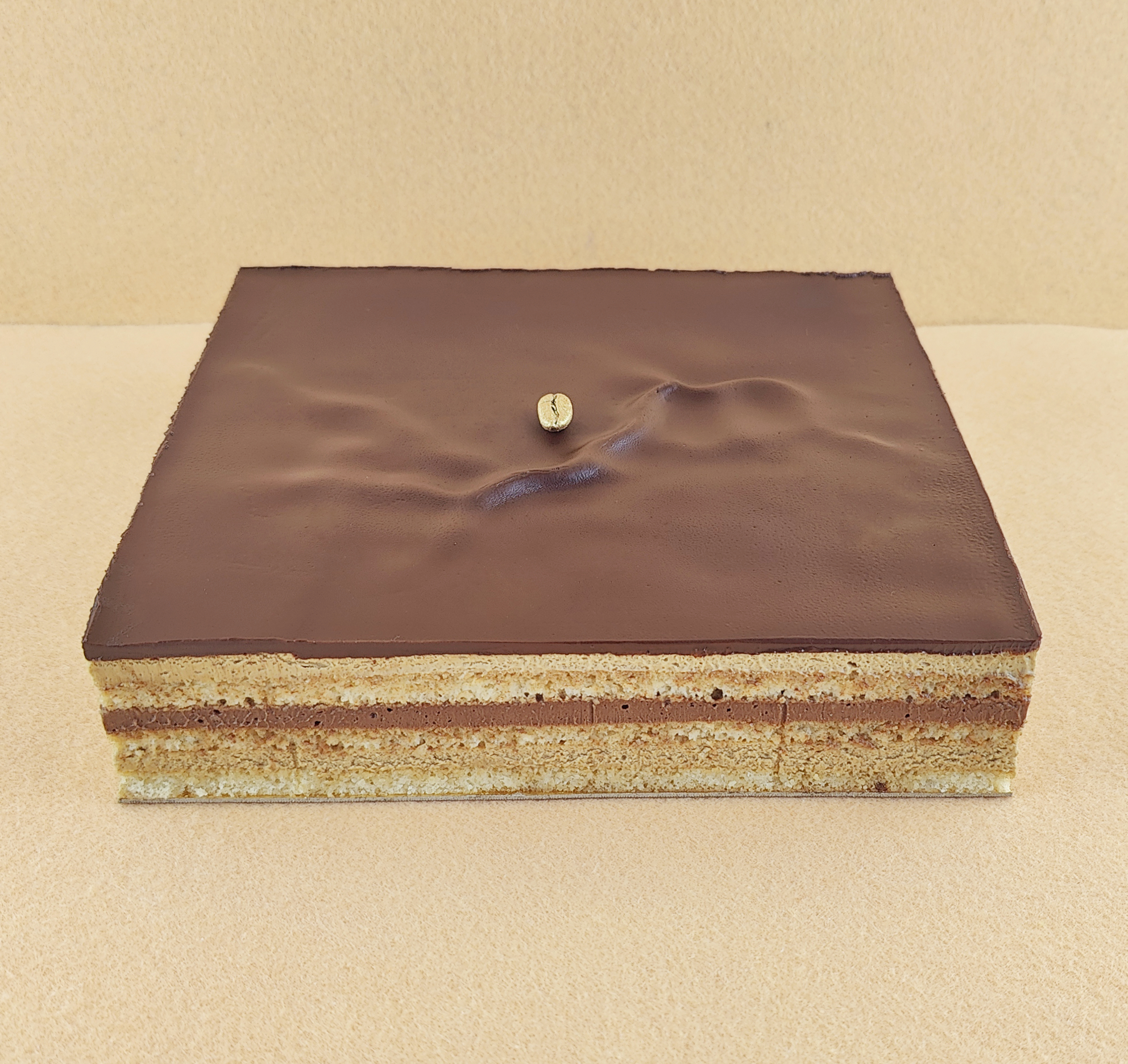 Tarta Ópera cuadrada para varias personas, fotografiada en ángulo de 45 grados, con cobertura de chocolate, cortes limpios donde se aprecian todas las capas y granos de café decorativos en la superficie.