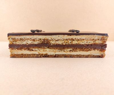 Tarta Ópera cuadrada vista de frente, mostrando claramente las capas alternas de bizcocho de almendra, crema de café y ganache de chocolate, con granos de café decorando la parte superior.