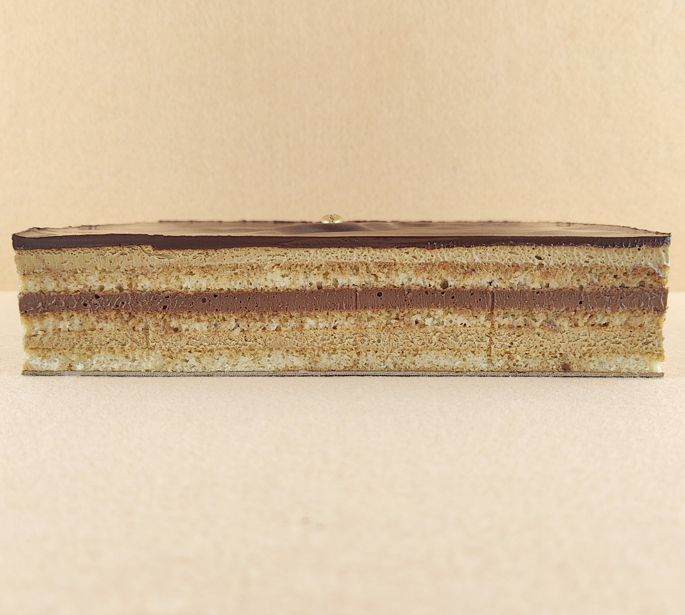 Tarta Ópera cuadrada vista de frente, mostrando claramente las capas alternas de bizcocho de almendra, crema de café y ganache de chocolate, con granos de café decorando la parte superior.