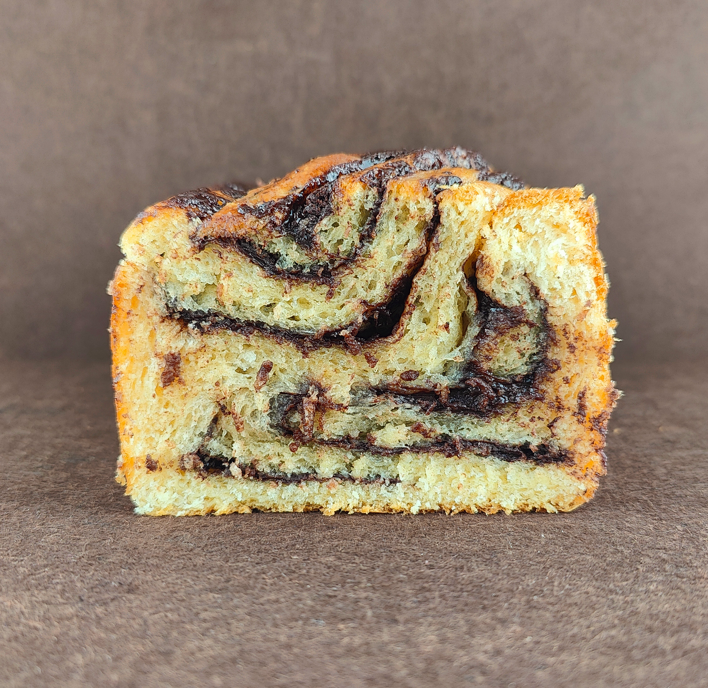 Babka de chocolate vista desde arriba sobre fondo marrón claro, mostrando el trenzado de la masa de brioche y las capas de crema de chocolate.