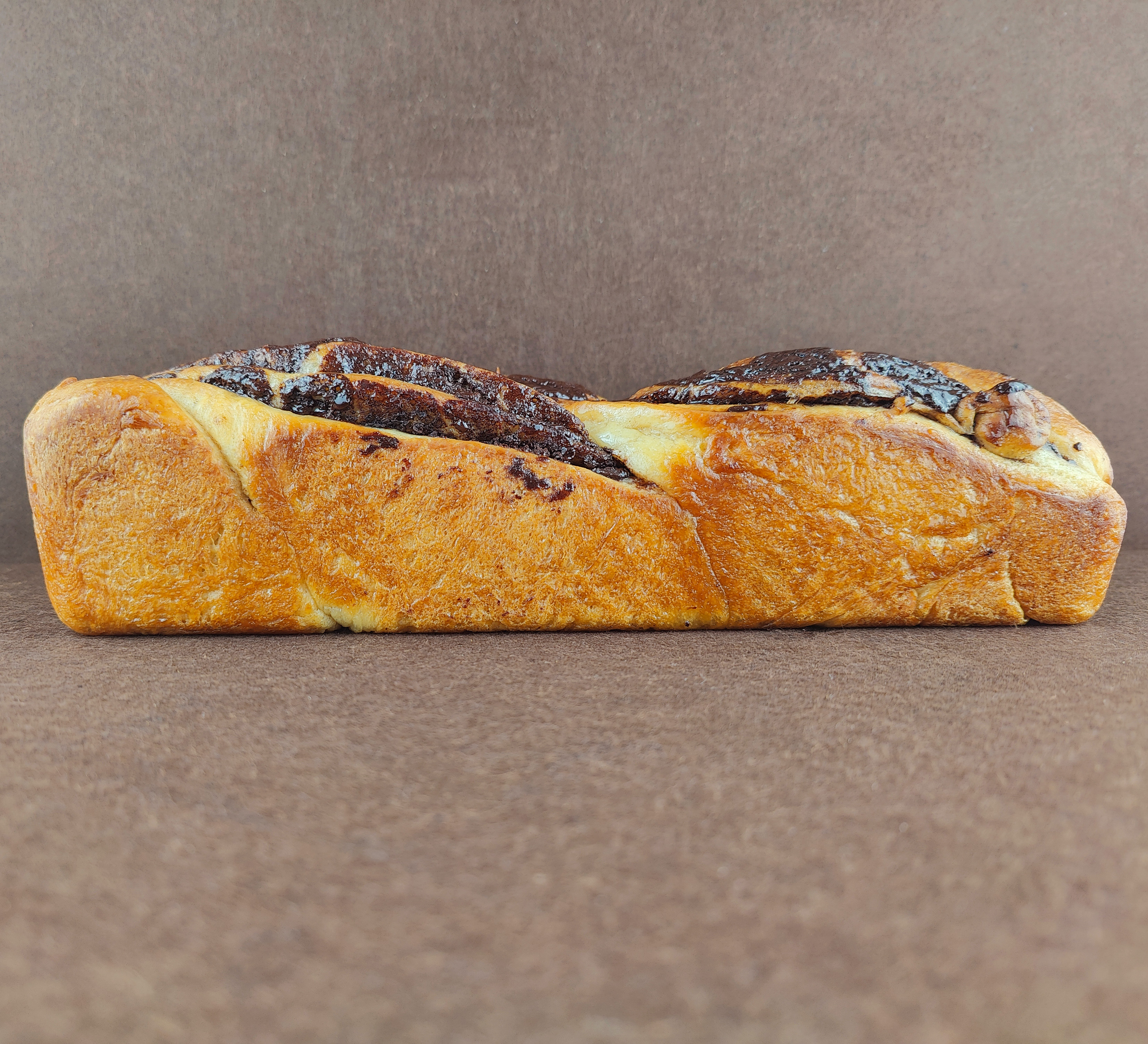 Babka de chocolate cortada sobre fondo marrón claro, mostrando la miga tierna de brioche y el relleno de crema de chocolate en el interior.