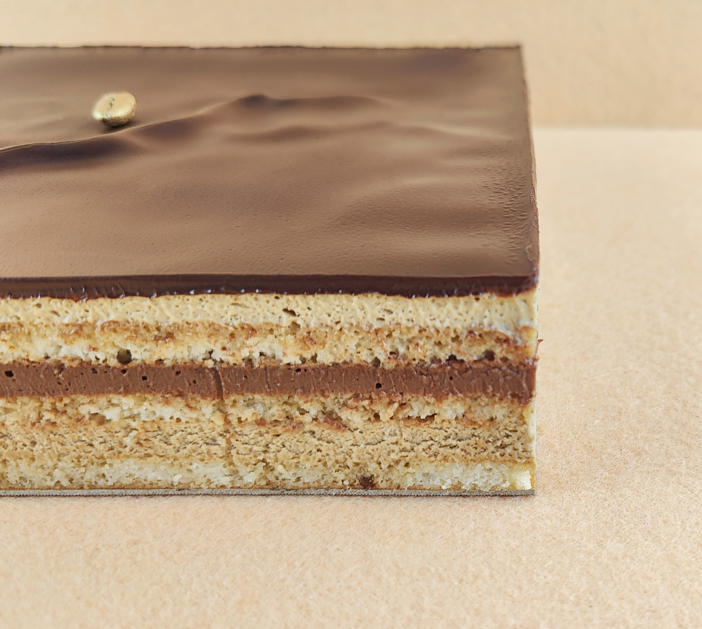 Primer plano de una Tarta Ópera cuadrada, resaltando la textura de la cobertura de chocolate, la suavidad de la crema de café, la cremosidad de la ganaché de chocolate y la esponjosidad del bizcocho gioconda empapado en café.