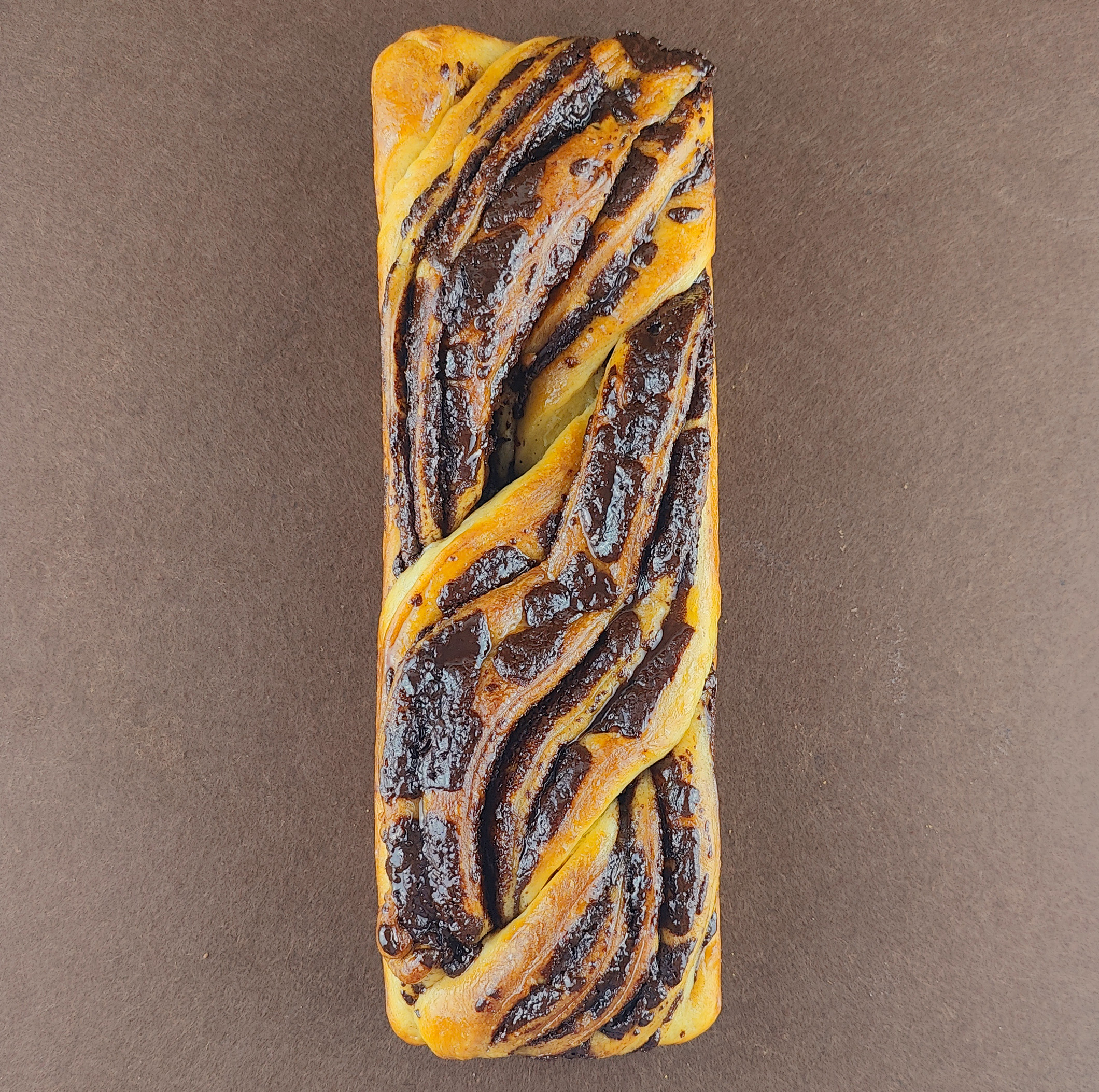 Detalle cercano de la Babka de chocolate sobre fondo marrón claro, resaltando el trenzado, el relleno de chocolate y el brillo del glaseado de agua de azahar.
