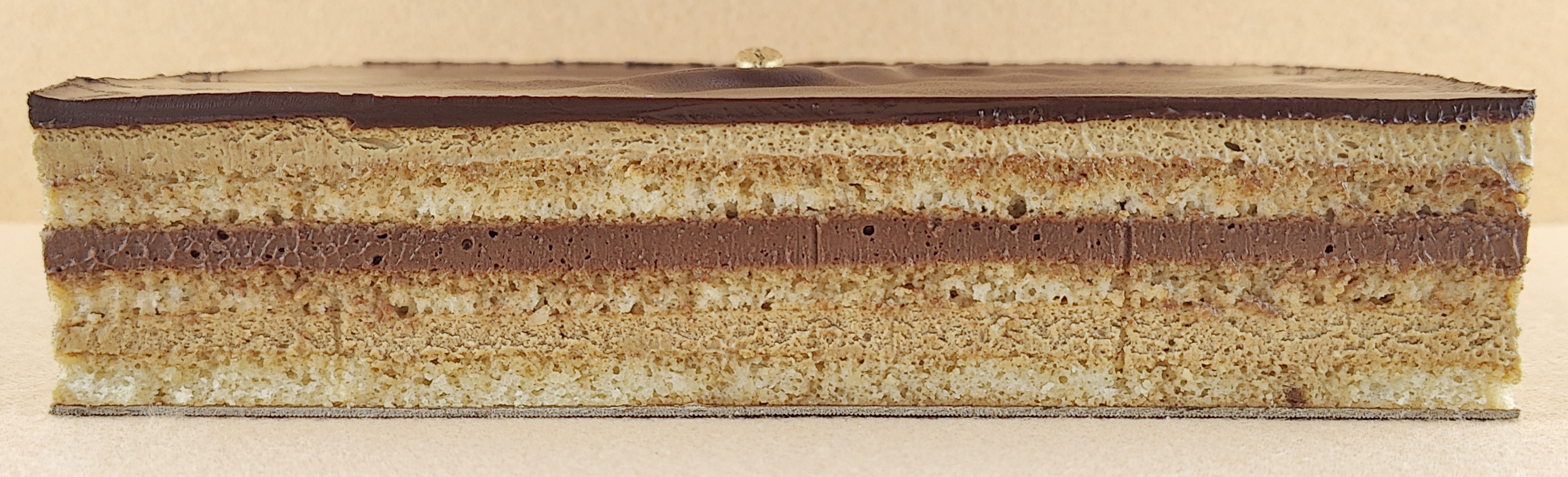 Porción individual rectangular de Tarta Ópera vista de frente, con sus capas alternas de bizcocho de almendra, crema de café y ganache de chocolate perfectamente alineadas.
