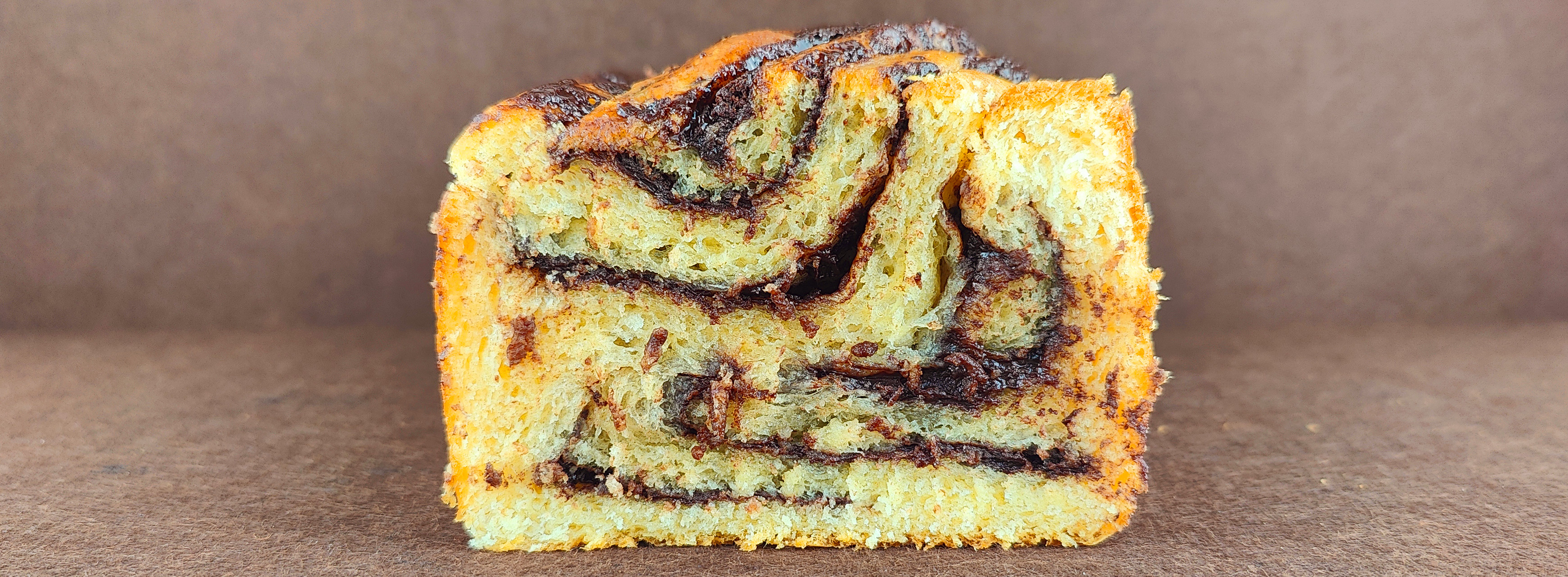 Babka de chocolate vista desde arriba sobre fondo marrón claro, mostrando el trenzado de la masa de brioche y las capas de crema de chocolate.