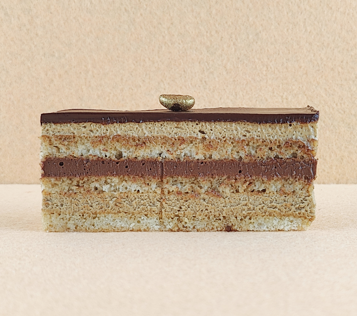 Primer plano de una porción rectangular de Tarta Ópera, destacando la textura lisa de la cobertura de chocolate y la definición de las capas de bizcocho de almendra, crema de café y ganache de chocolate.