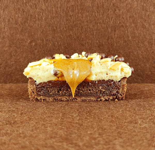 Porción individual rectangular de Tarta Ópera vista de frente, con sus capas alternas de bizcocho de almendra, crema de café y ganache de chocolate perfectamente alineadas.