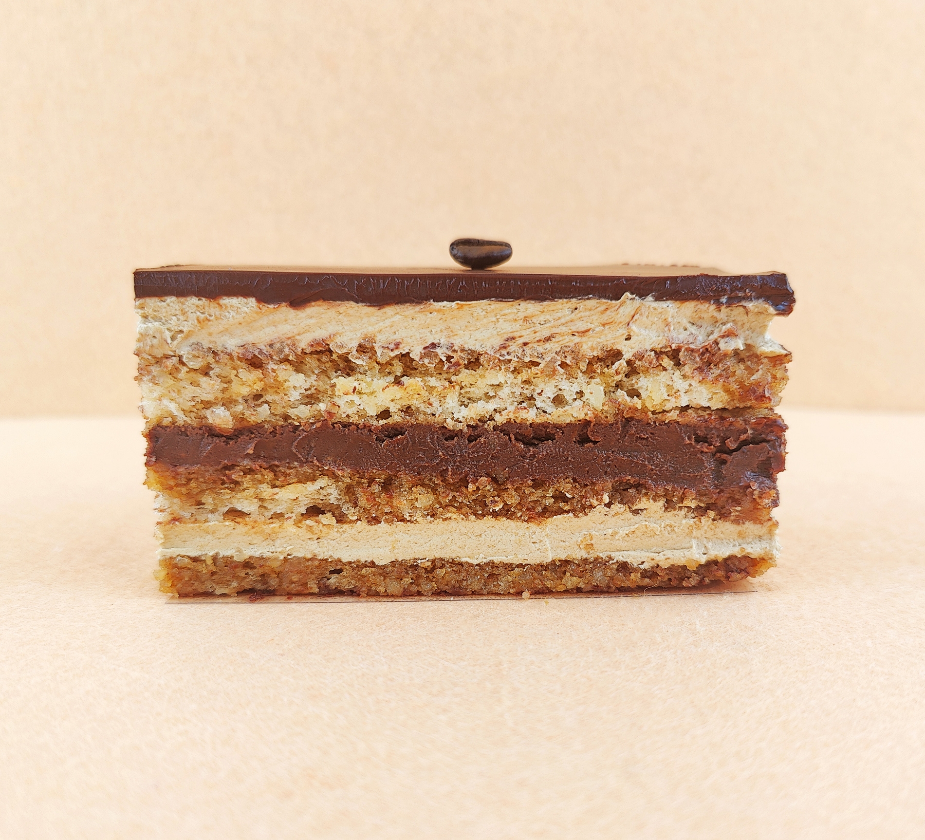 Porción individual rectangular de Tarta Ópera vista de frente, con sus capas alternas de bizcocho de almendra, crema de café y ganache de chocolate perfectamente alineadas.