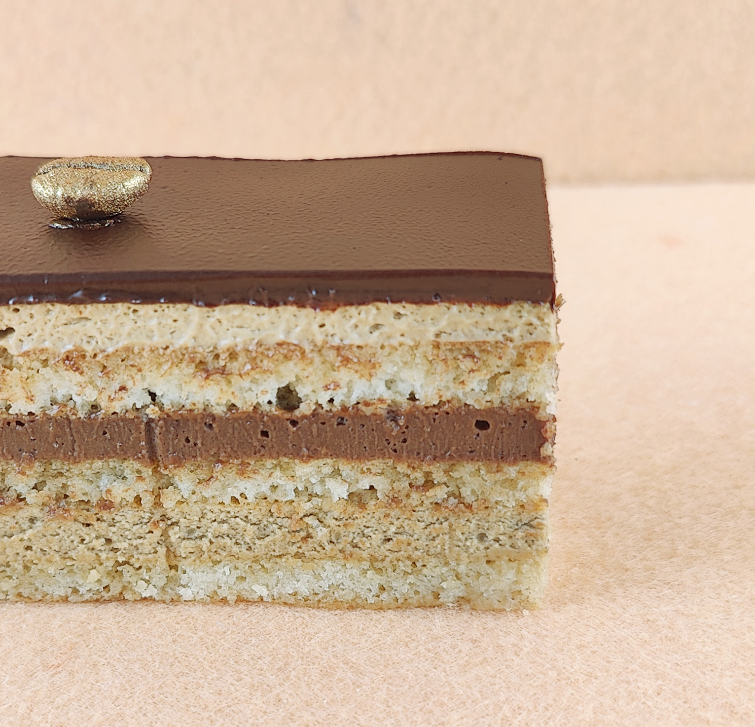 Porción individual rectangular de Tarta Ópera vista de frente, con sus capas alternas de bizcocho de almendra, crema de café y ganache de chocolate perfectamente alineadas.